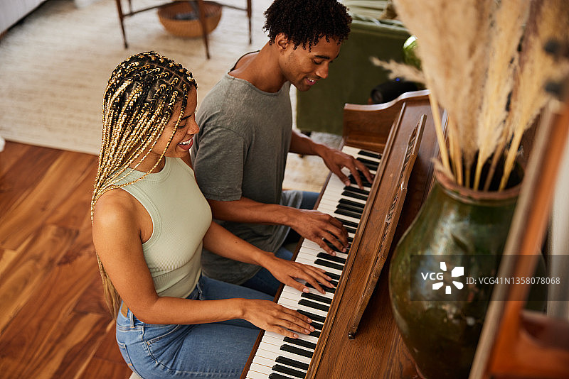 年轻情侣在家一起弹钢琴，面带微笑图片素材