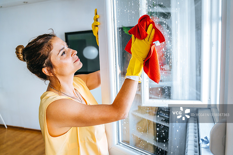 年轻女子用喷雾瓶和抹布清洁窗户图片素材