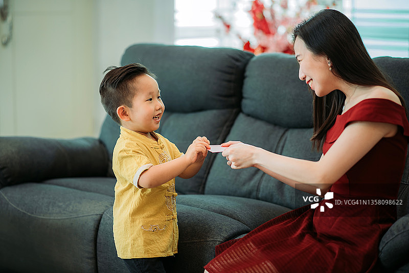 中国新年期间，亚洲可爱男孩在客厅里收到表亲的红包图片素材