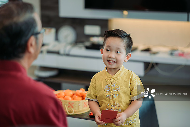 中国春节：亚洲男孩从爷爷那里接过红包，喜笑颜开图片素材