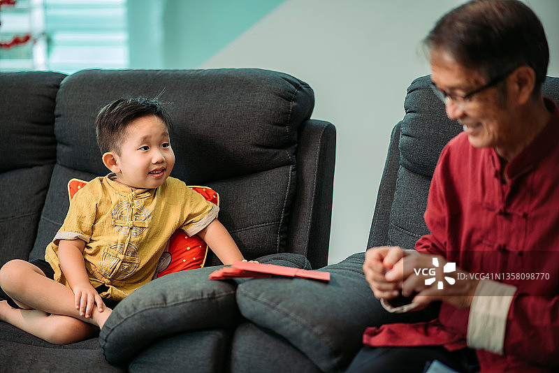 中国祖孙春节期间在客厅，孙子看着爷爷包红包图片素材