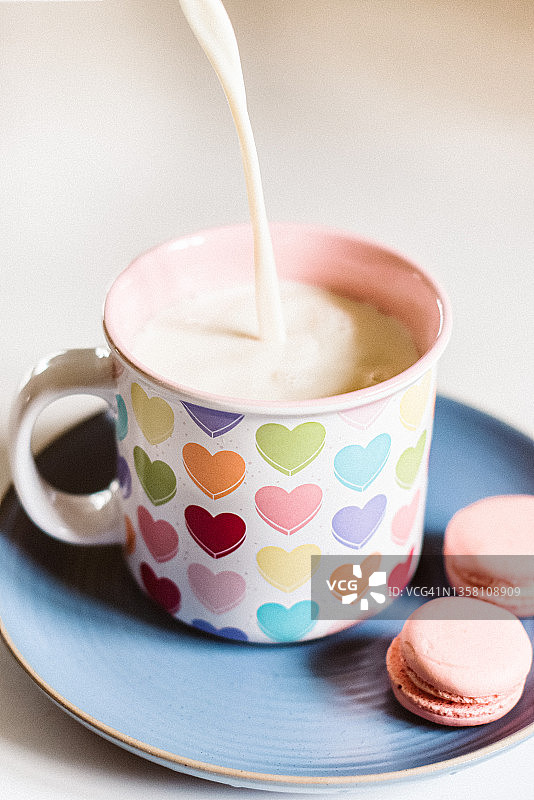 不含乳糖的牛奶倒入杯中，杯子放在绿松石盘子上，旁边放着两个纯素马卡龙图片素材