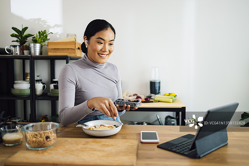 微笑的女人在厨房做健康早餐时进行视频通话图片素材