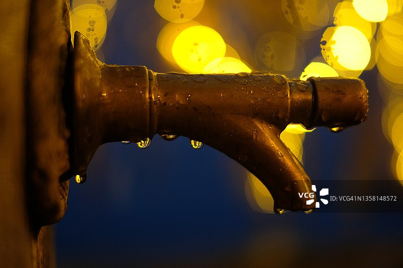 雨湿黄铜水龙头与模糊的背景灯图片素材