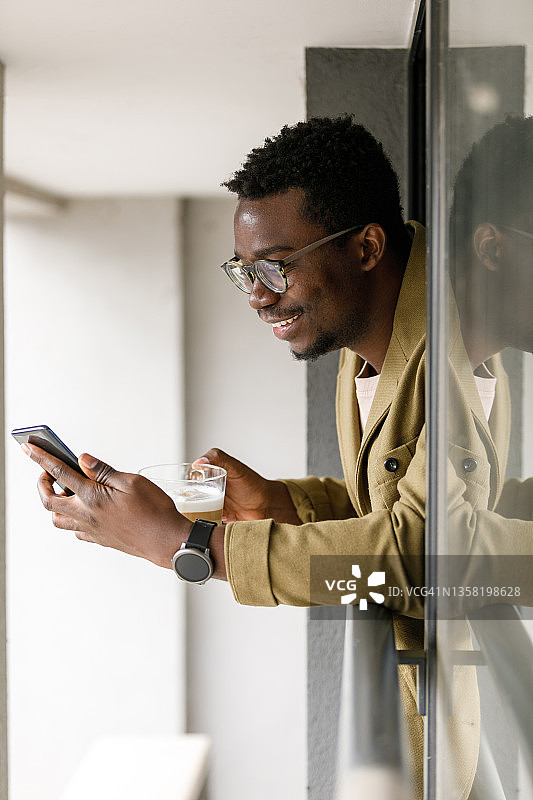 商务人士倚靠着窗户，用智能手机喝咖啡图片素材