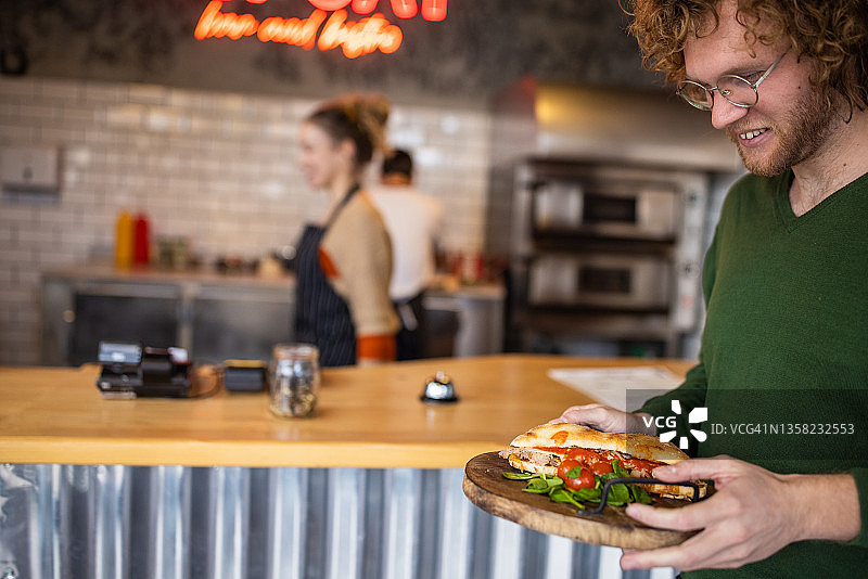 笑容满面的男顾客从快餐店取走他点的三明治图片素材