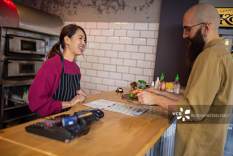 快乐的日裔女雇员为白人男顾客提供食物图片素材