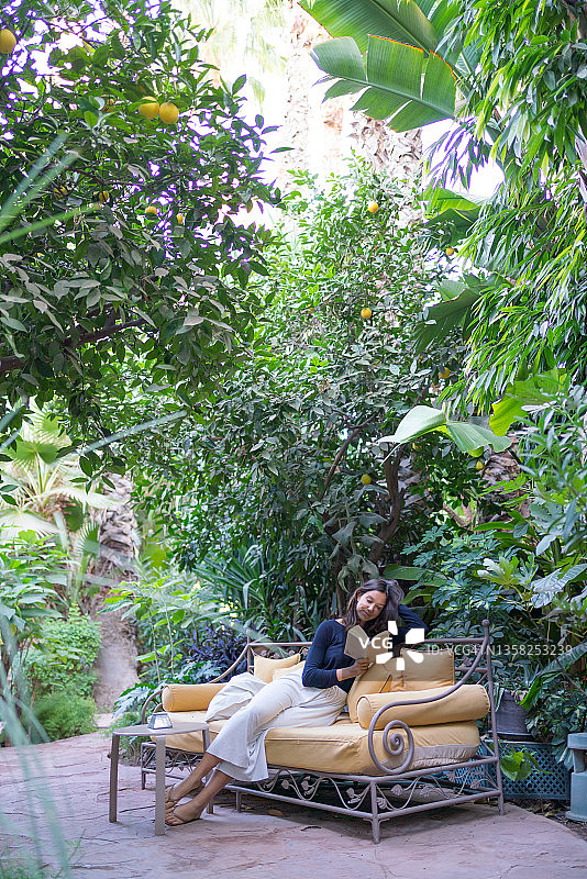 年轻女人在花园沙发上看书放松图片素材