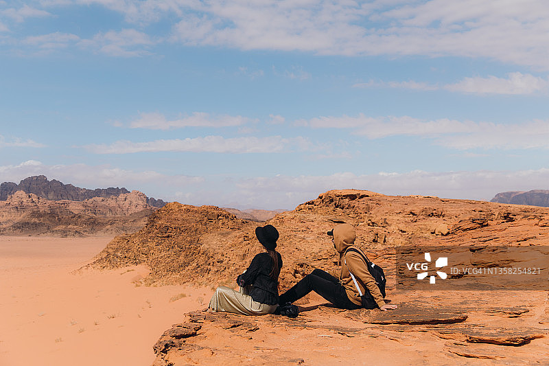 年轻女人和男人探险家正在欣赏瓦迪拉姆沙漠的风景图片素材
