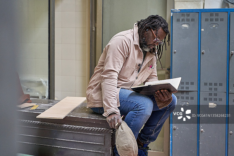 中年非裔美国建筑工人在旧桌旁坐着，一边看笔记本上的笔记图片素材