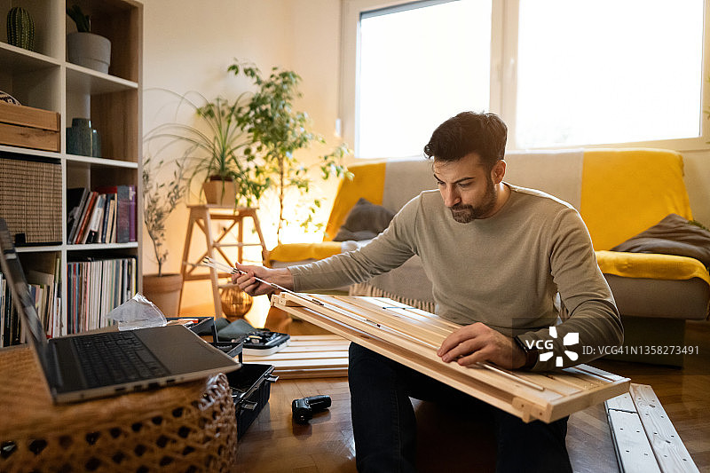 组装家具时，男性工匠在笔记本电脑上观看在线教程图片素材