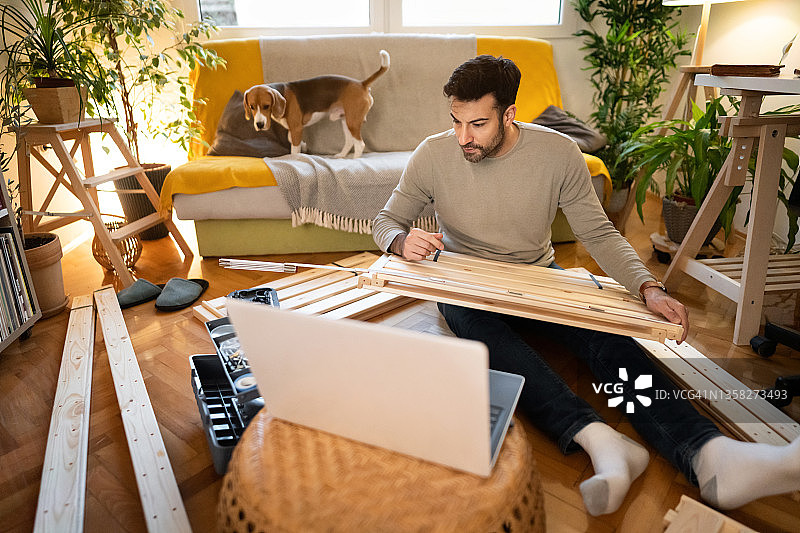 白人男子在组装家具时观看笔记本电脑上的DIY教程图片素材