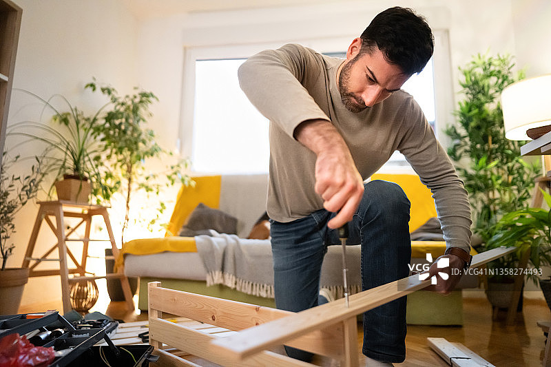 专注的白人男性工匠用螺丝刀在家组装家具图片素材