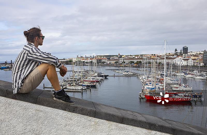 年轻男人坐在蓬塔德尔加达码头海滨。图片素材