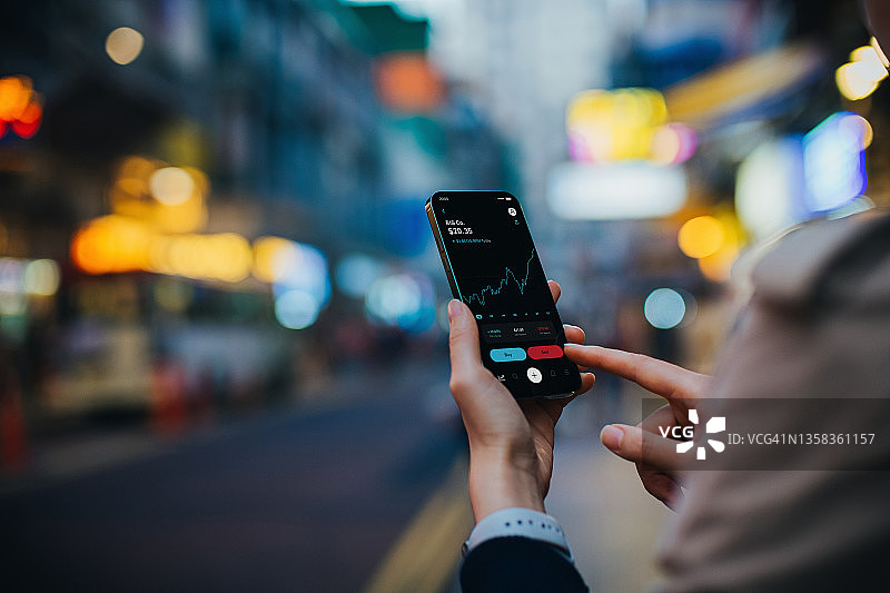 年轻亚裔女性在智能手机上管理金融股票交易的肩上视角图片素材