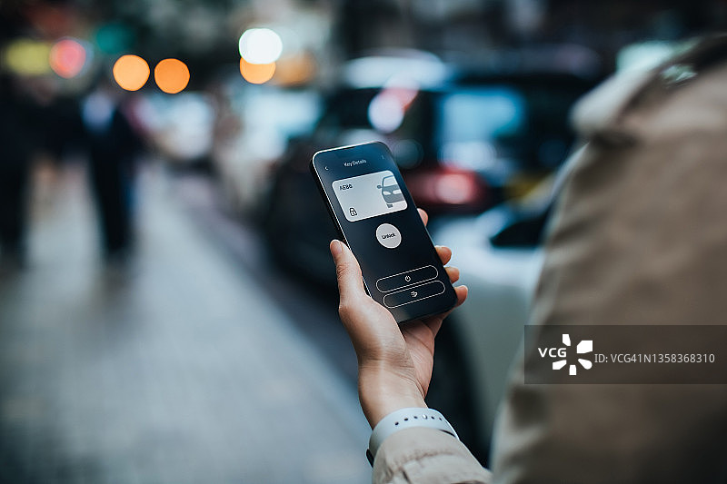 年轻亚洲女性在城市街道使用手机App解锁智能汽车图片素材
