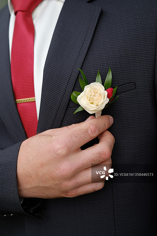 新郎身穿白色衬衫和黑色西装，胸前佩戴着白色花朵和绿色叶子的胸花，婚礼主题图片素材