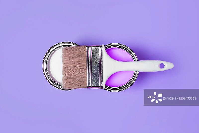 一把干净的画笔放在两个金属桶上，桶里装着粉色霓虹灯和白色油漆，用于在长春花蓝色背景上进行翻新工程。扁平风格。为您的设计提供复制空间。展示2022年家居室内色彩的概念。设计用配色样本图片素材