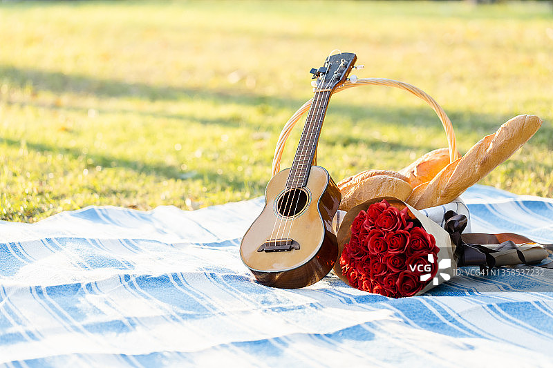 野餐垫上的尤克里里琴和红玫瑰，野餐装饰图片素材