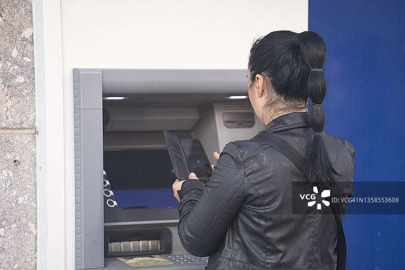 女人使用非接触式手机在ATM机上操作照片图片素材