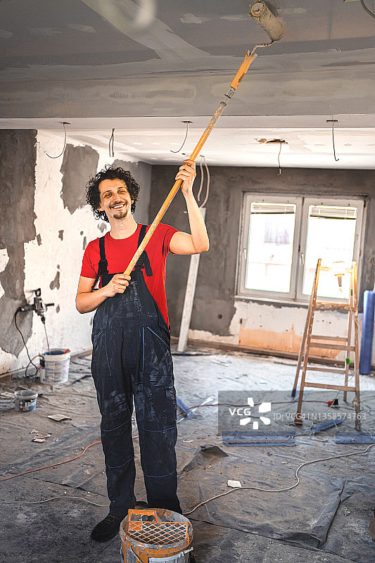 笑容满面的建筑工人粉刷公寓墙壁的肖像图片素材