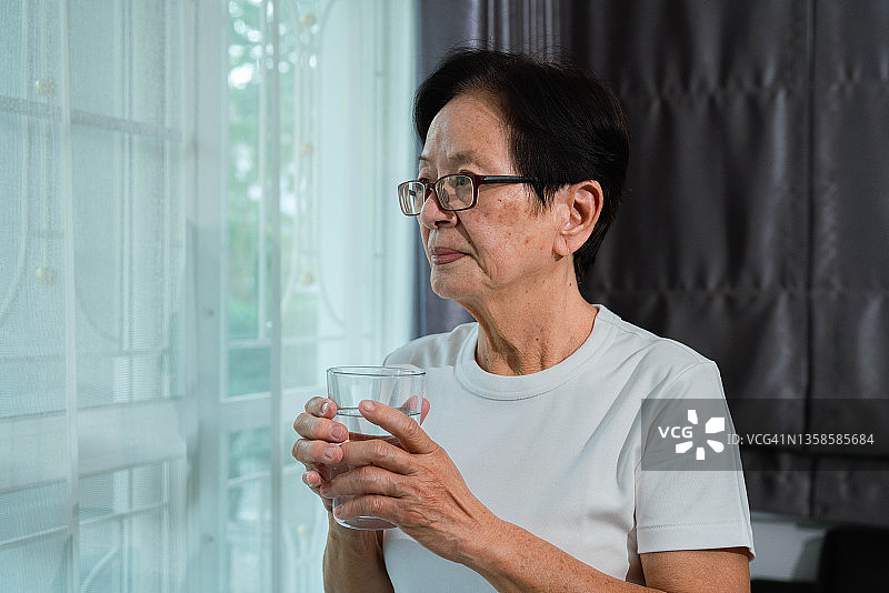 亚洲年长妇女拿着一杯水。图片素材