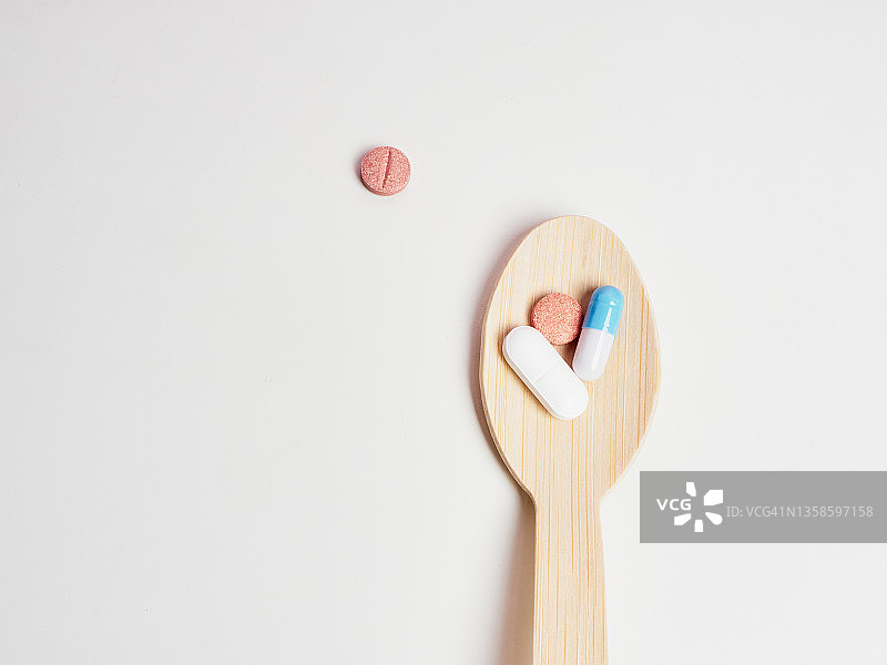 装有药丸和胶囊的木勺，白色桌面图片素材