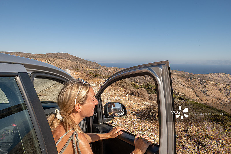 年轻女子下车欣赏希腊岛屿的海滩全景，公路旅行概念图片素材