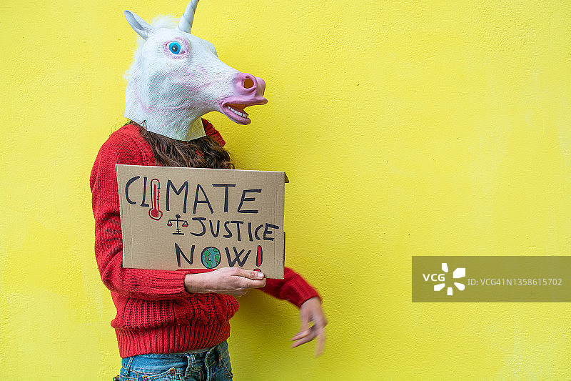 戴着独角兽面具，手持气候正义标语的女人图片素材