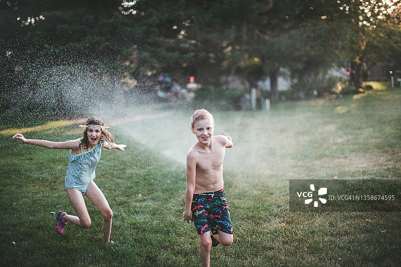 在草坪洒水器下玩耍的儿童图片素材