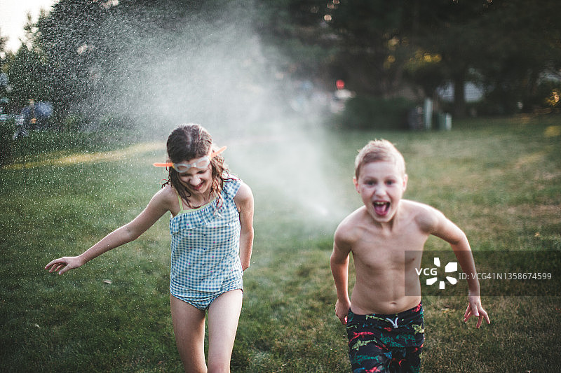 在草坪洒水器下玩耍的儿童图片素材