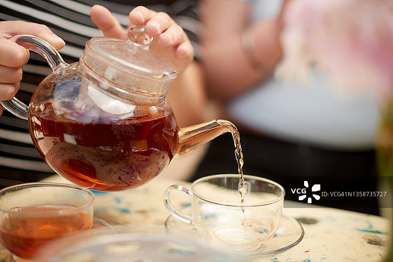 一名女子为自己和朋友倒茶图片素材