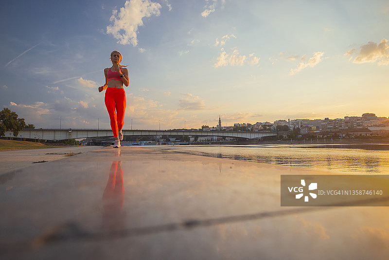 中年妇女穿着运动装在黄昏的河边跑步图片素材