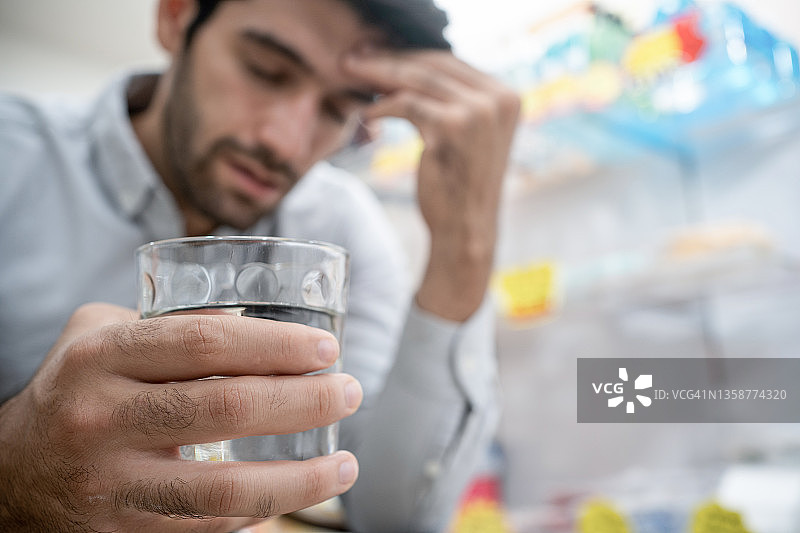 年轻男人在床上拿水杯，手扶额头，可能头痛或宿醉图片素材