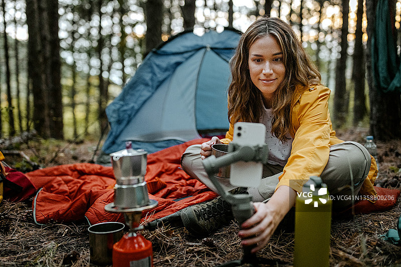 笑容满面的女人喝着咖啡，使用智能手机图片素材