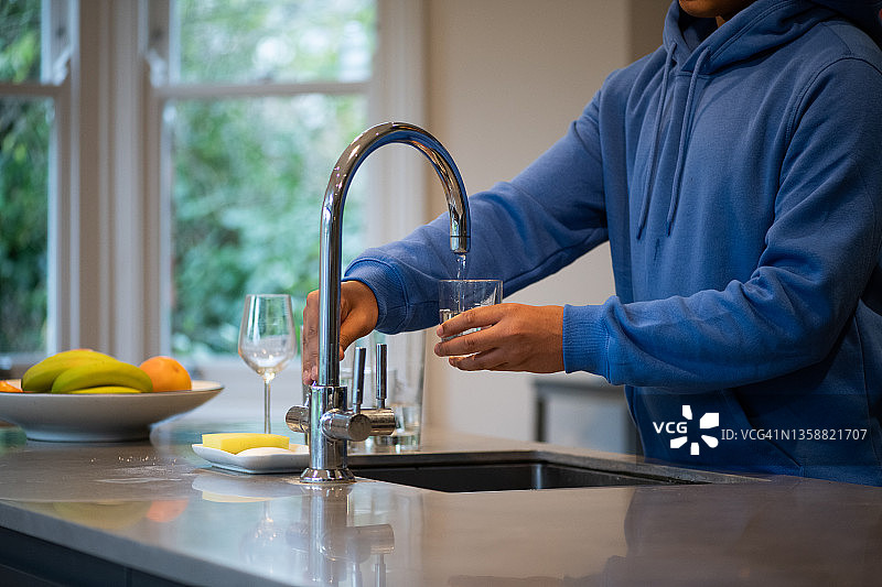 年轻男人从水龙头往玻璃杯里倒水图片素材