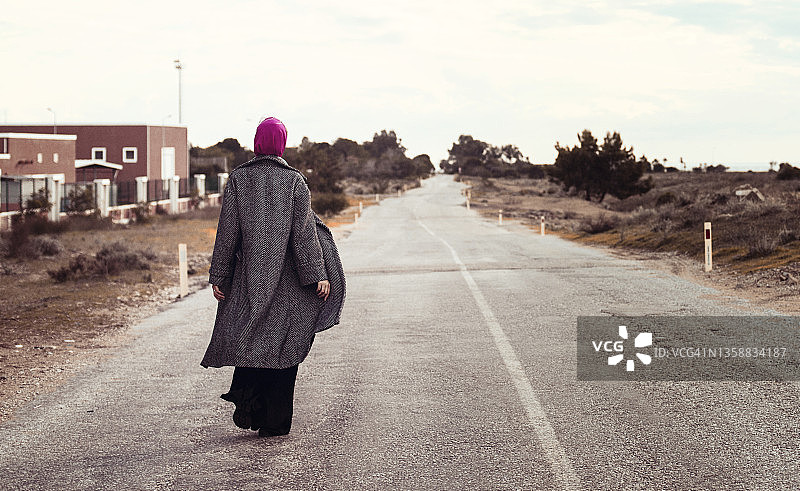 围着围巾、穿着长外套，独自走在空旷道路上的女人图片素材