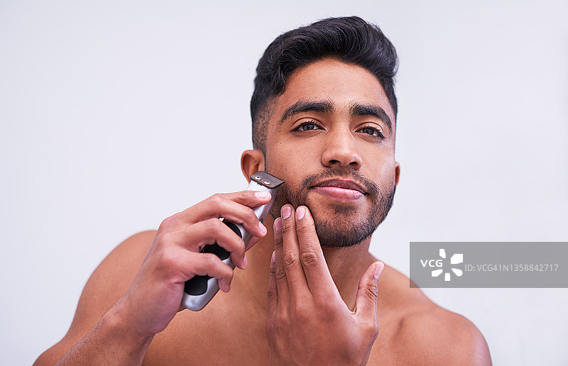 年轻男子在白色背景下使用电动剃须刀图片素材