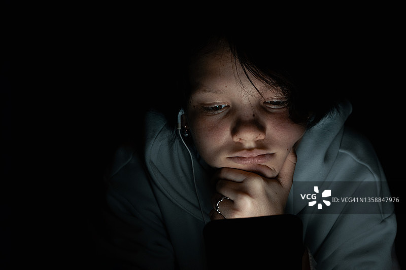 疲惫的少女深夜戴着耳机使用智能手机图片素材