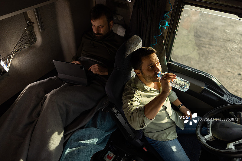 卡车司机坐在驾驶室里接受医疗，他的同事躺在后面的床上图片素材