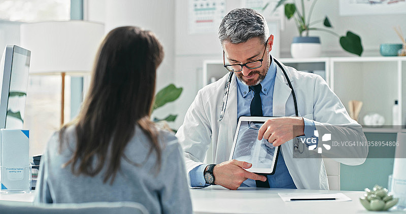 年长的医生和病人坐在一起，在平板电脑上向她展示X光片图片素材