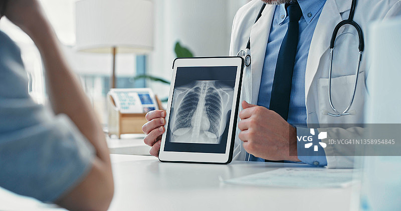 身份不明的医生与病人坐在一起，在平板电脑上向她展示X光片的局部照片图片素材