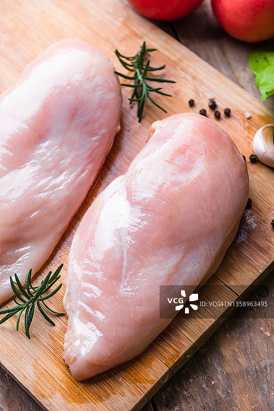 木质背景上带有迷迭香和香料的生鸡胸肉片图片素材