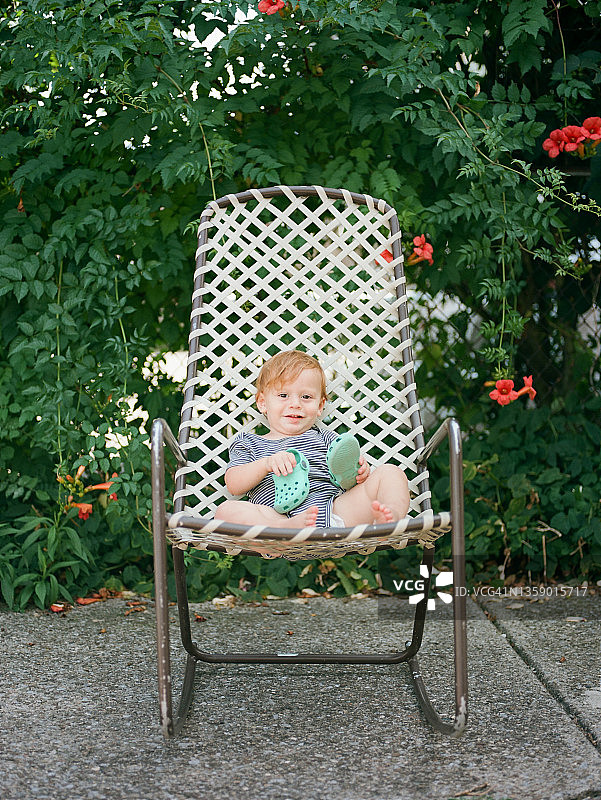 夏日里，穿着连体衣坐在后院摇椅上的小红发幼儿男孩图片素材