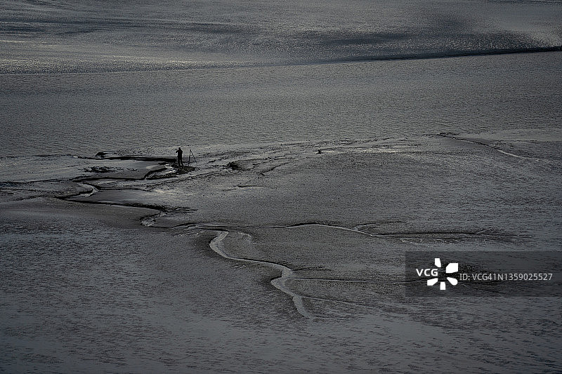 独自等待在圣米歇尔山退潮时潮间带水域沙滩上的摄影师图片素材