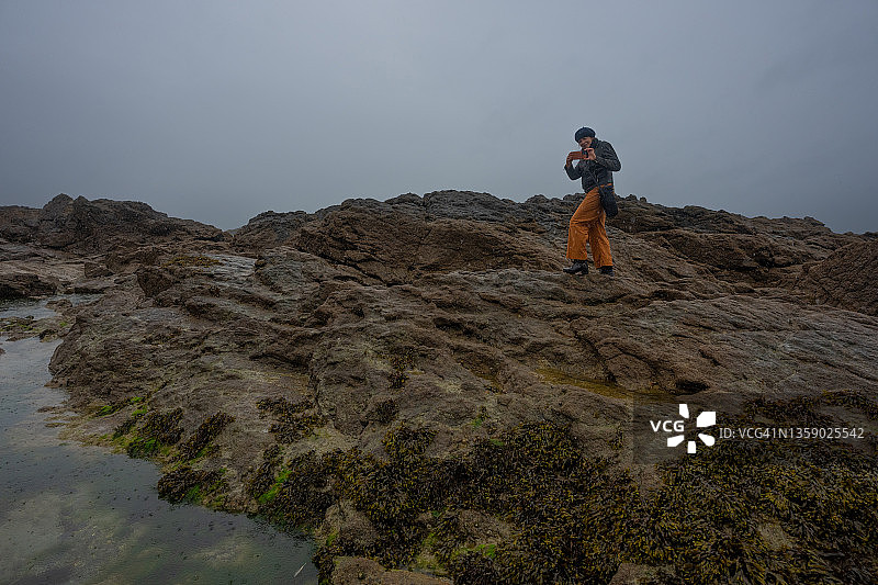 一位女士在圣马洛的岩石海滩和潮汐池用手机拍照图片素材