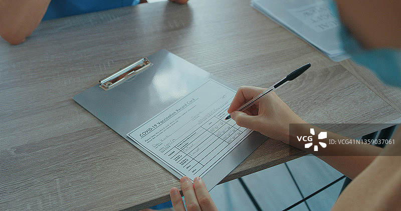 一位无法辨认的医生在诊所签署疫苗卡图片素材