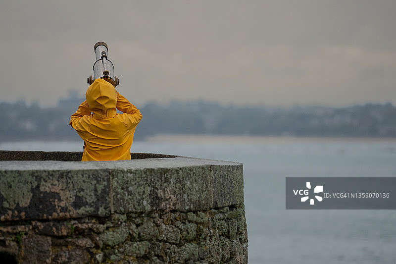 身穿黄色雨衣，用望远镜观看的年轻人图片素材