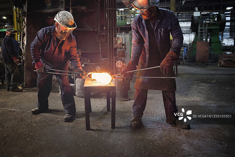 锻造工人将钢坯交给同事进行曲轴锻造图片素材
