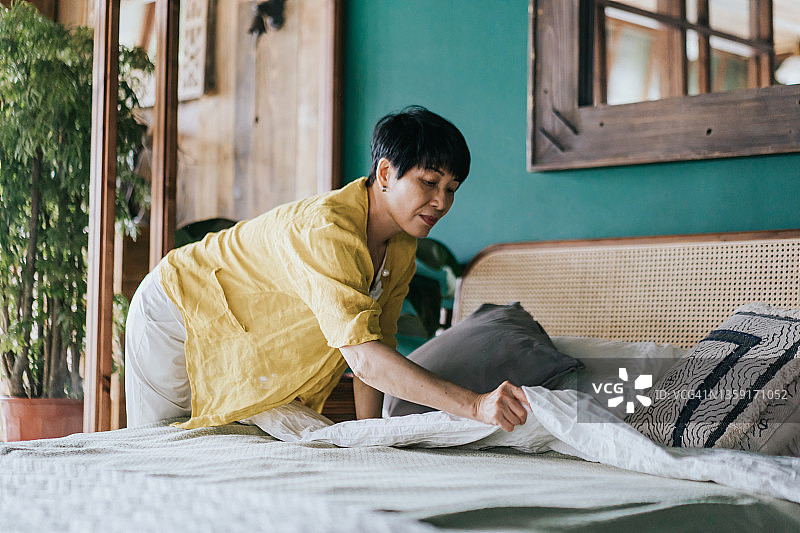 年长的亚洲妇女做她的早晨例行公事，在家里整理她的床。让我们开始新的一天图片素材